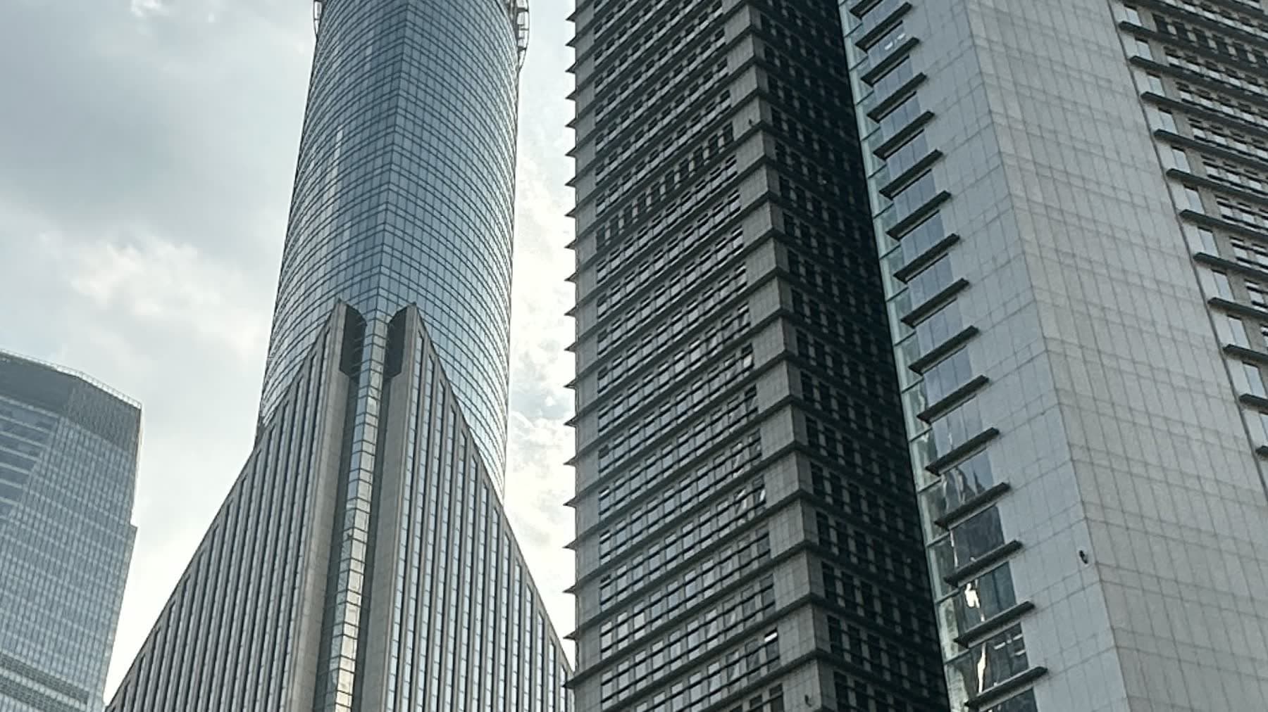 Modern glass and stone towers rising against a pale sky, seen from street level.